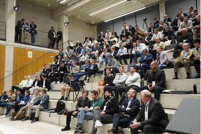 A large audience sits on tiered steps in a modern auditorium during an event.