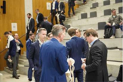Attendees in business attire gather and talk near the steps after a session.