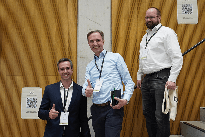 Three attendees smile and give thumbs-up while standing on auditorium steps.