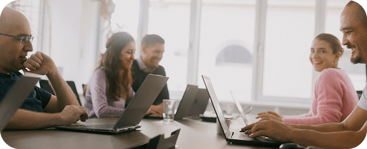 Smiling team members working together on laptops in a bright, modern office, fostering a collaborative and positive work environment.