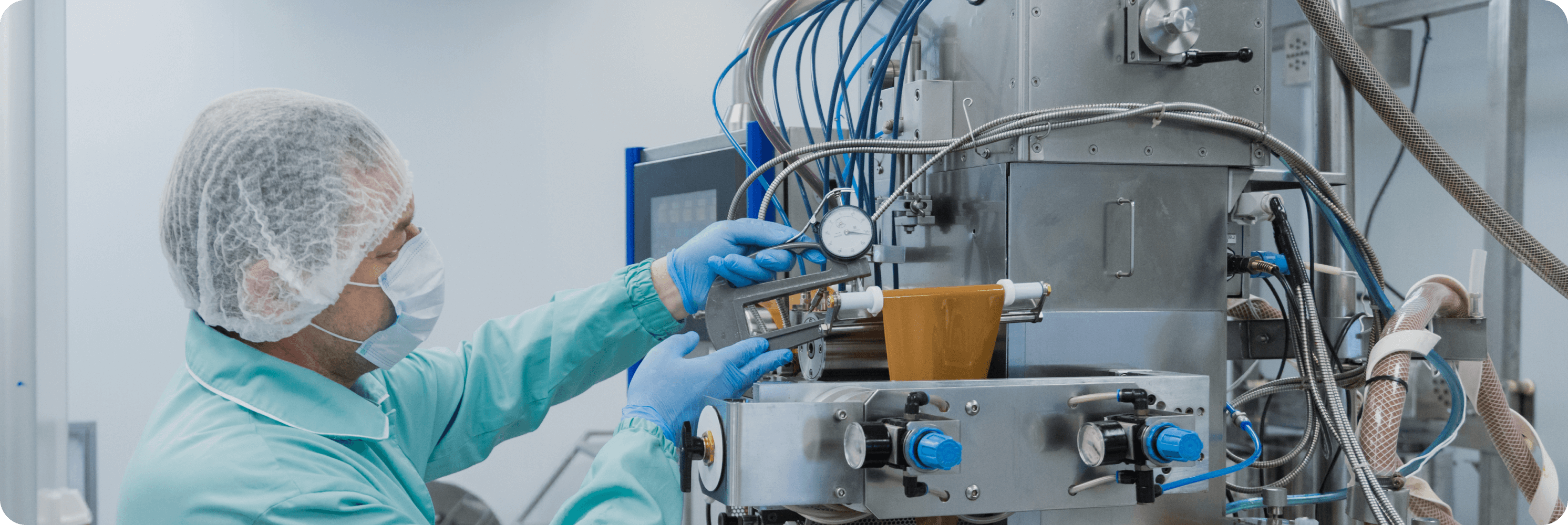 Pharmaceutical technician wearing a lab gown and mask operating complex stainless steel equipment in a cleanroom environment