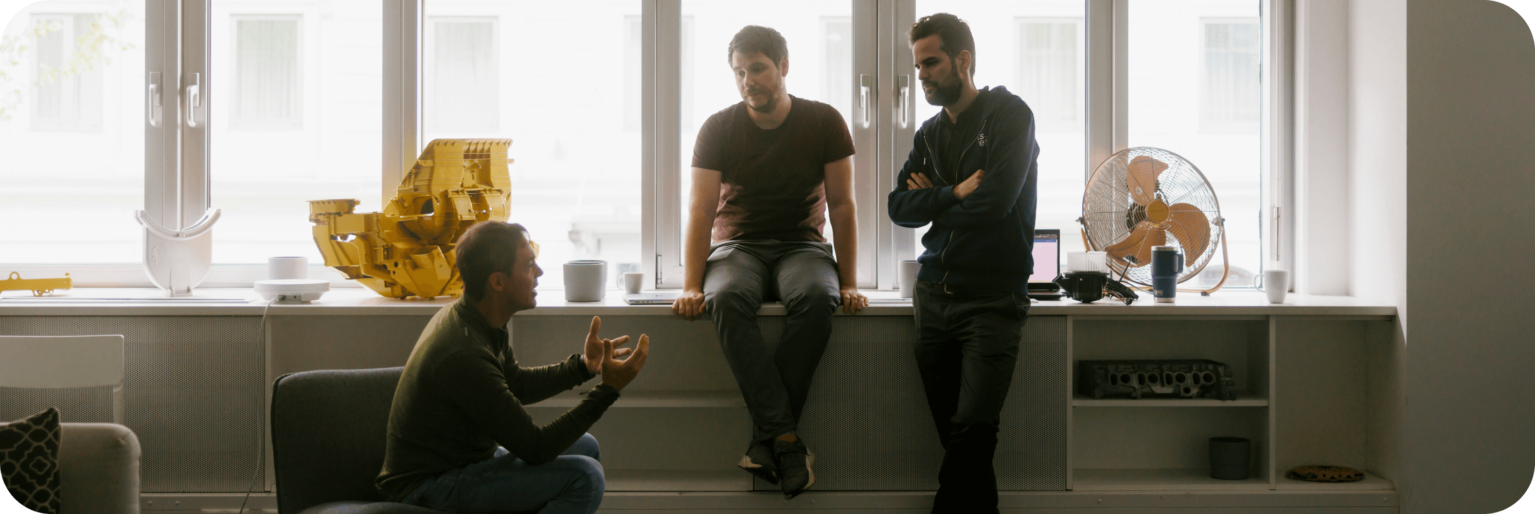 Colleagues having a technical discussion by the window with industrial part prototypes on display