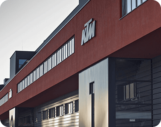 Außenansicht des KTM-Hauptquartiers mit seiner charakteristischen rot-schwarzen Fassade, die die Innovation des Unternehmens in der Motorradherstellung demonstriert. Außenansicht des KTM-Hauptquartiers mit seiner charakteristischen rot-schwarzen Fassade, die die Innovation des Unternehmens in der Motorradherstellung demonstriert.