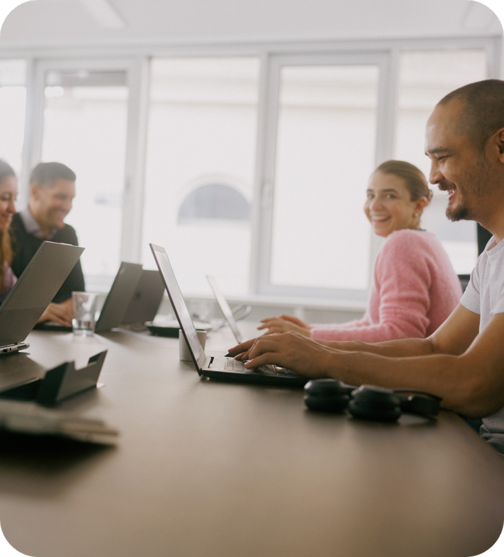 Four people sitting at the desk in from of their laptops and collaborating