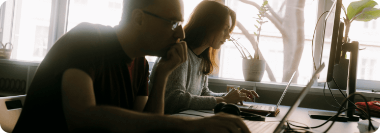 Two employees working intently at computers in a naturally lit workspace.