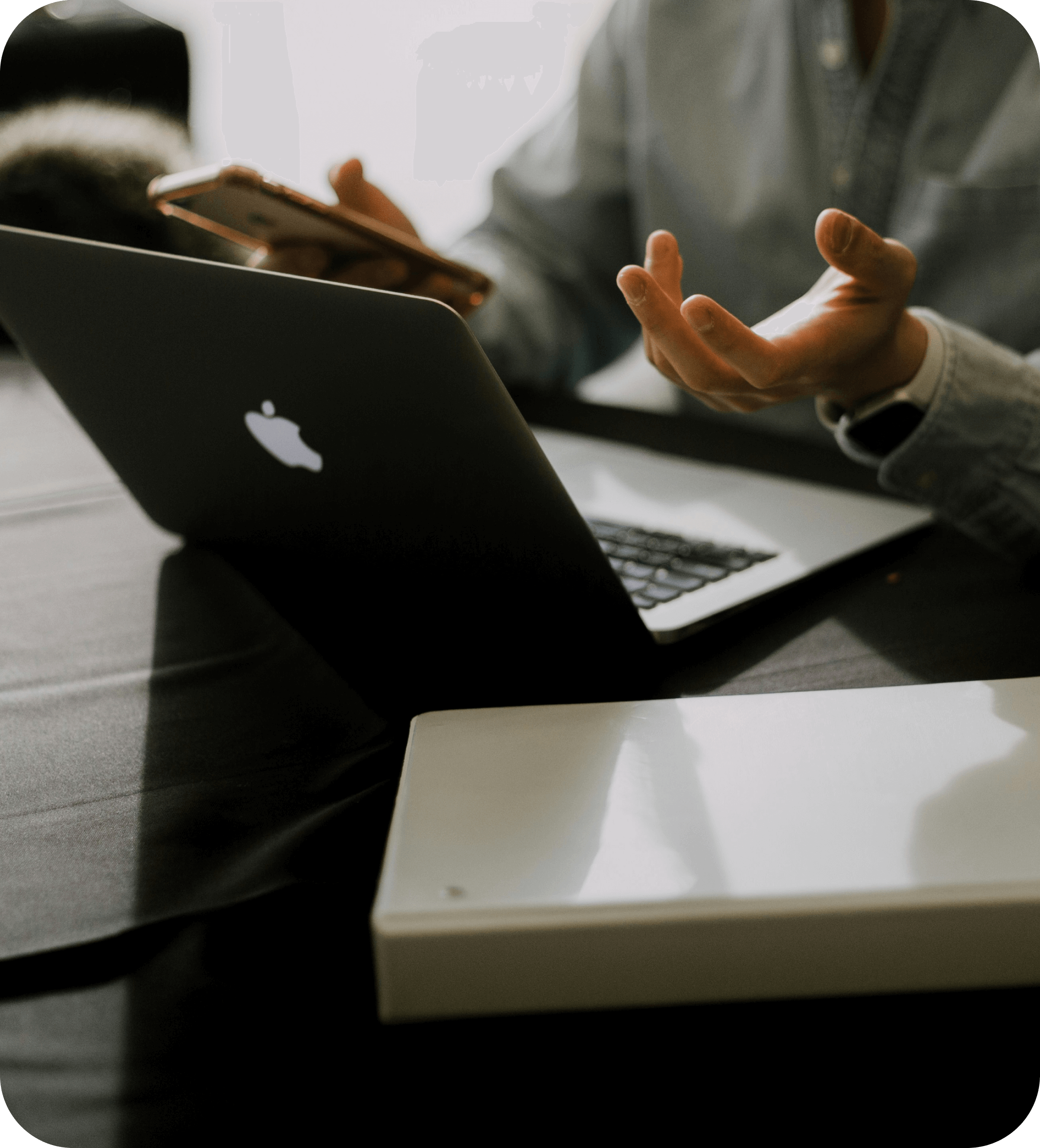 Person in business meeting using laptop and smartphone, representing cost engineering discussions and data-driven decision-making with product costing software