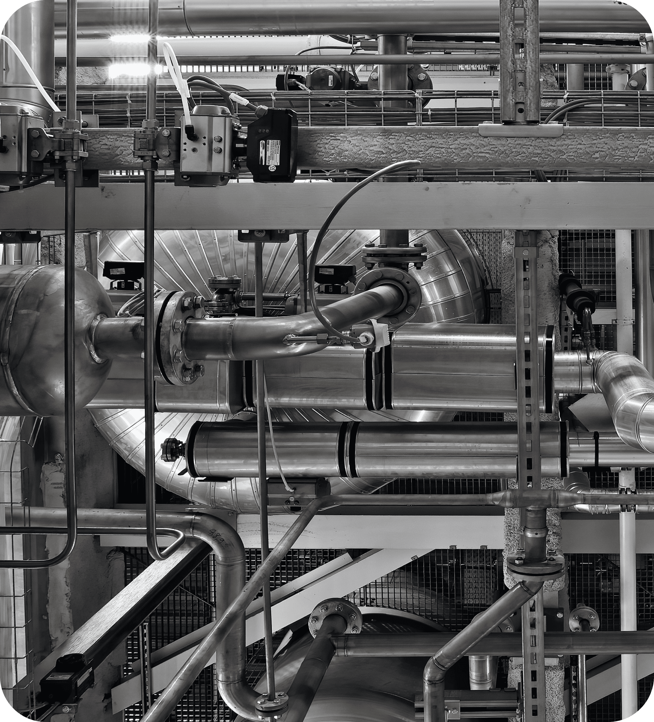 Black and white image of industrial piping and valves inside a manufacturing plant, representing energy systems and process engineering.
