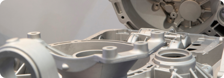 Close-up of gray metal engine components with intricate gear and bolt details. The industrial tone suggests precision engineering and manufacturing.